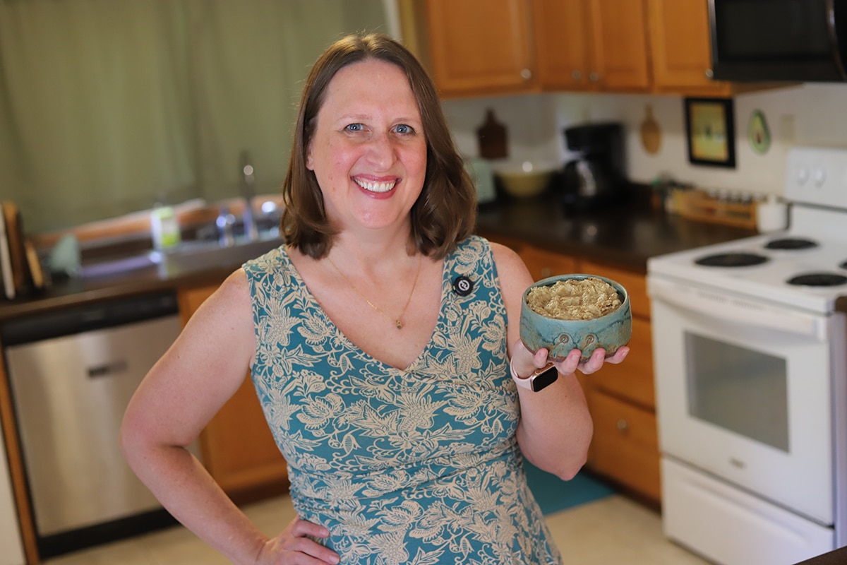 Cadry smiling in kitchen, holding bowl of baba ganoush eggplant dip.