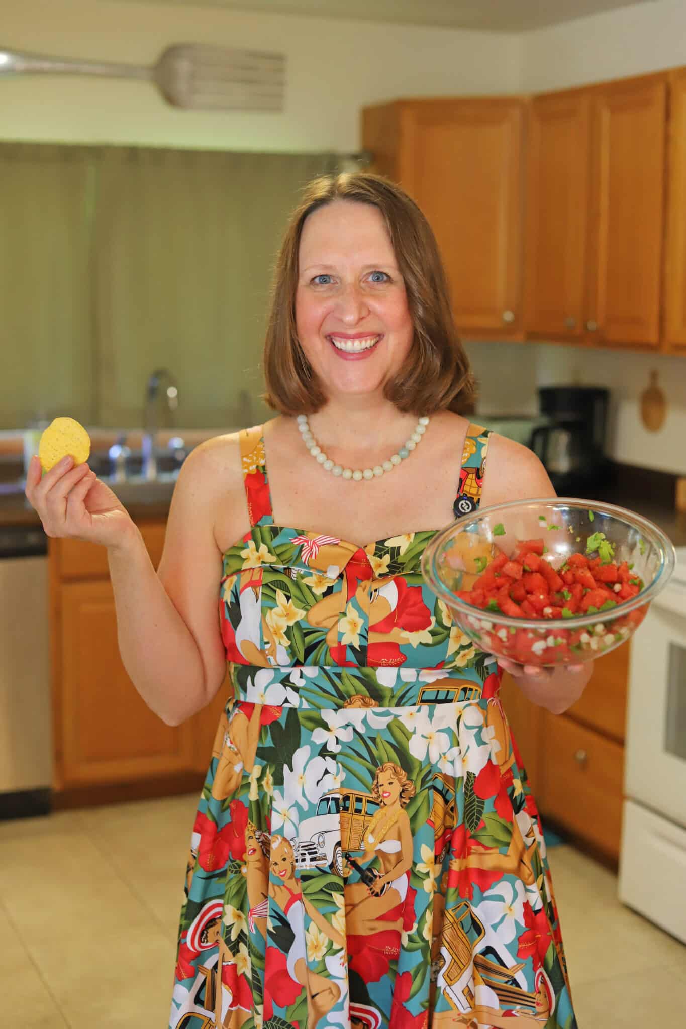 Cadry smiling in a colorful dress with a tortilla chip and bowl of watermelon salsa.