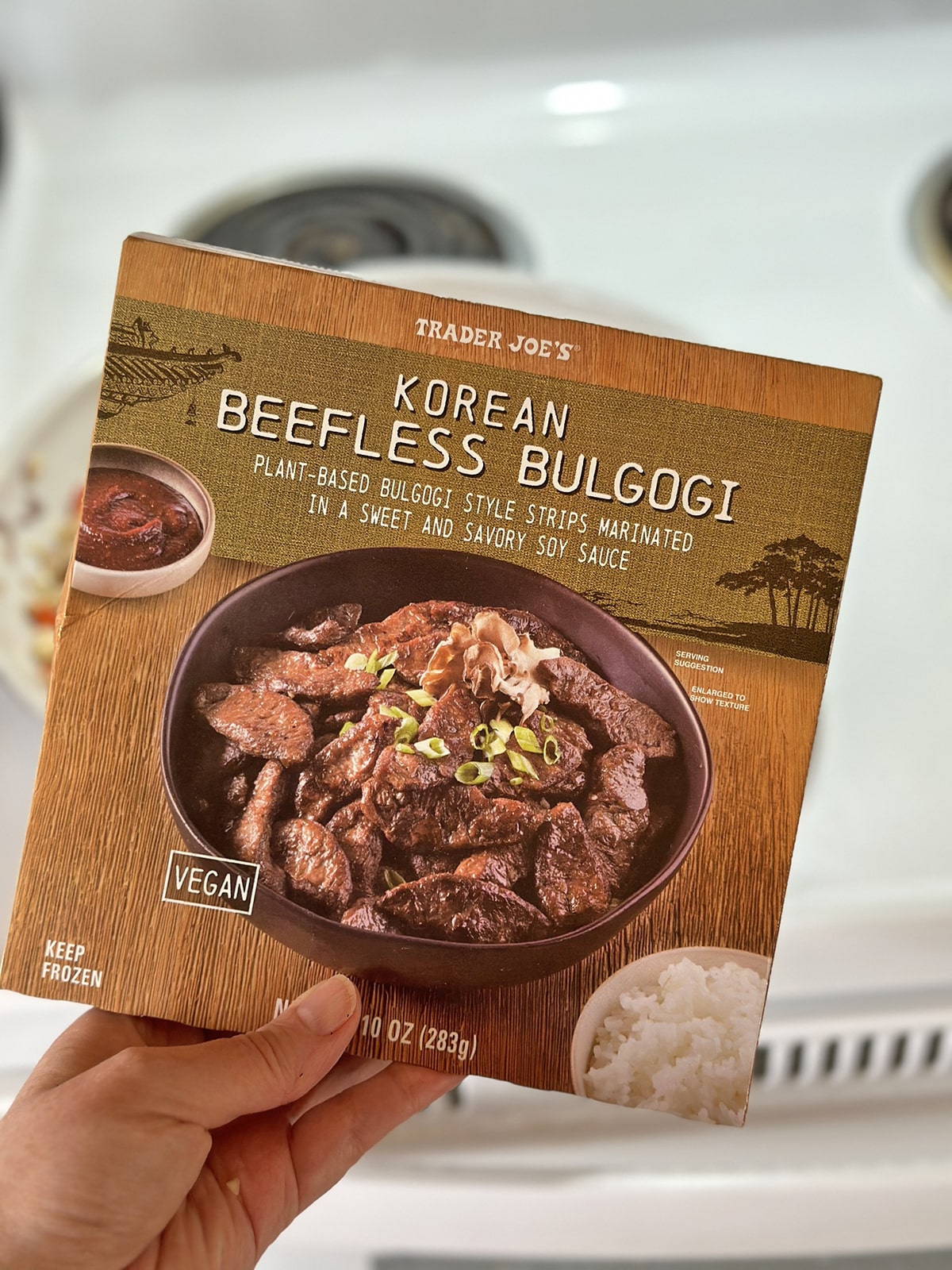 Hand holding package of Trader Joe's beefless bulgogi in front of stove.