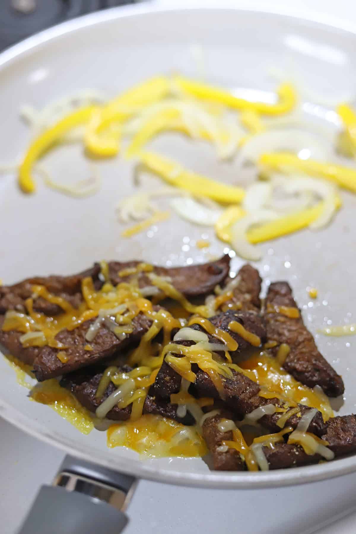 Non-dairy cheese melting on beefless bulgogi in skillet by peppers and onions.