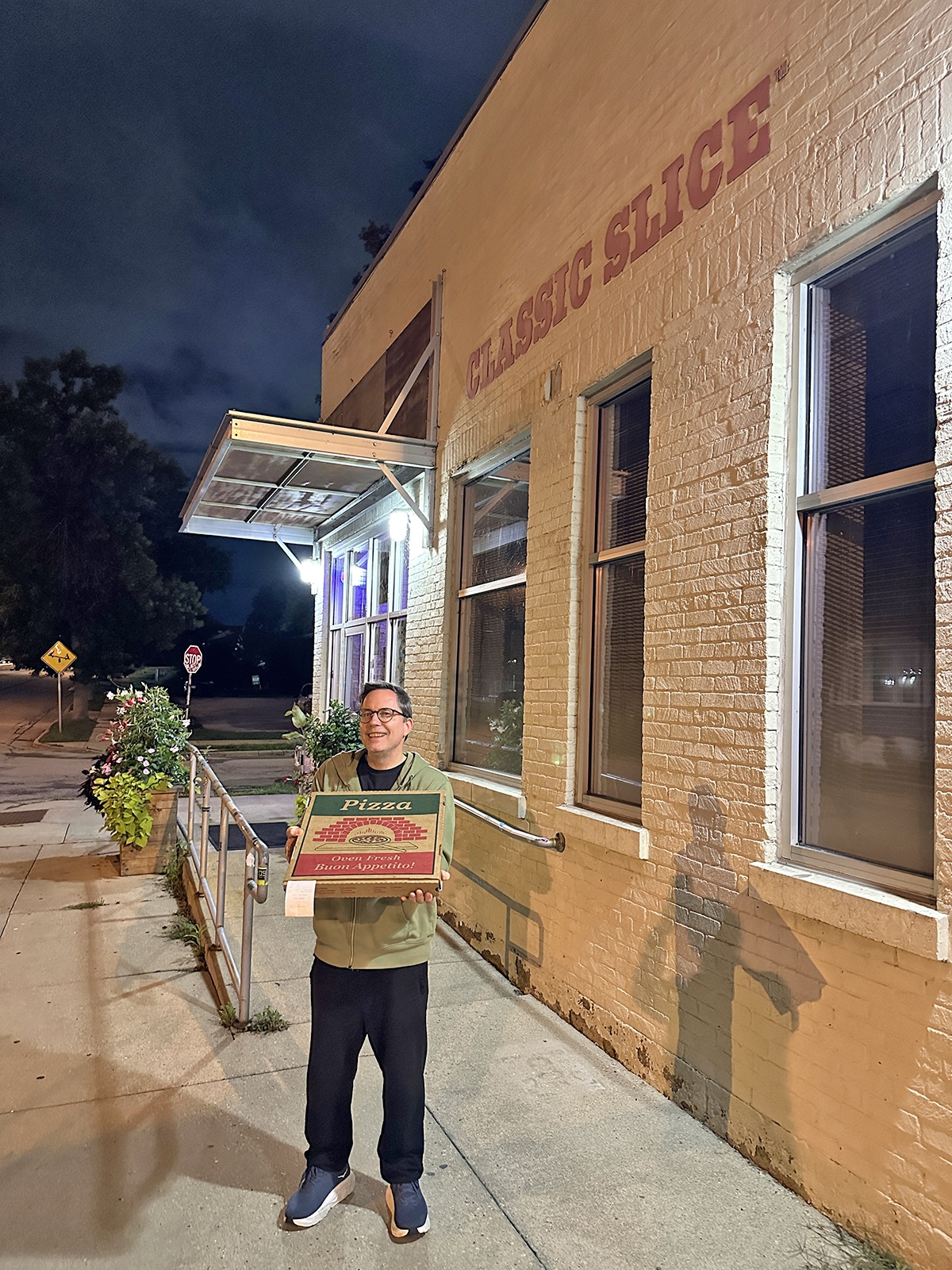 David holding box of pizza at night in front of Classic Slice.