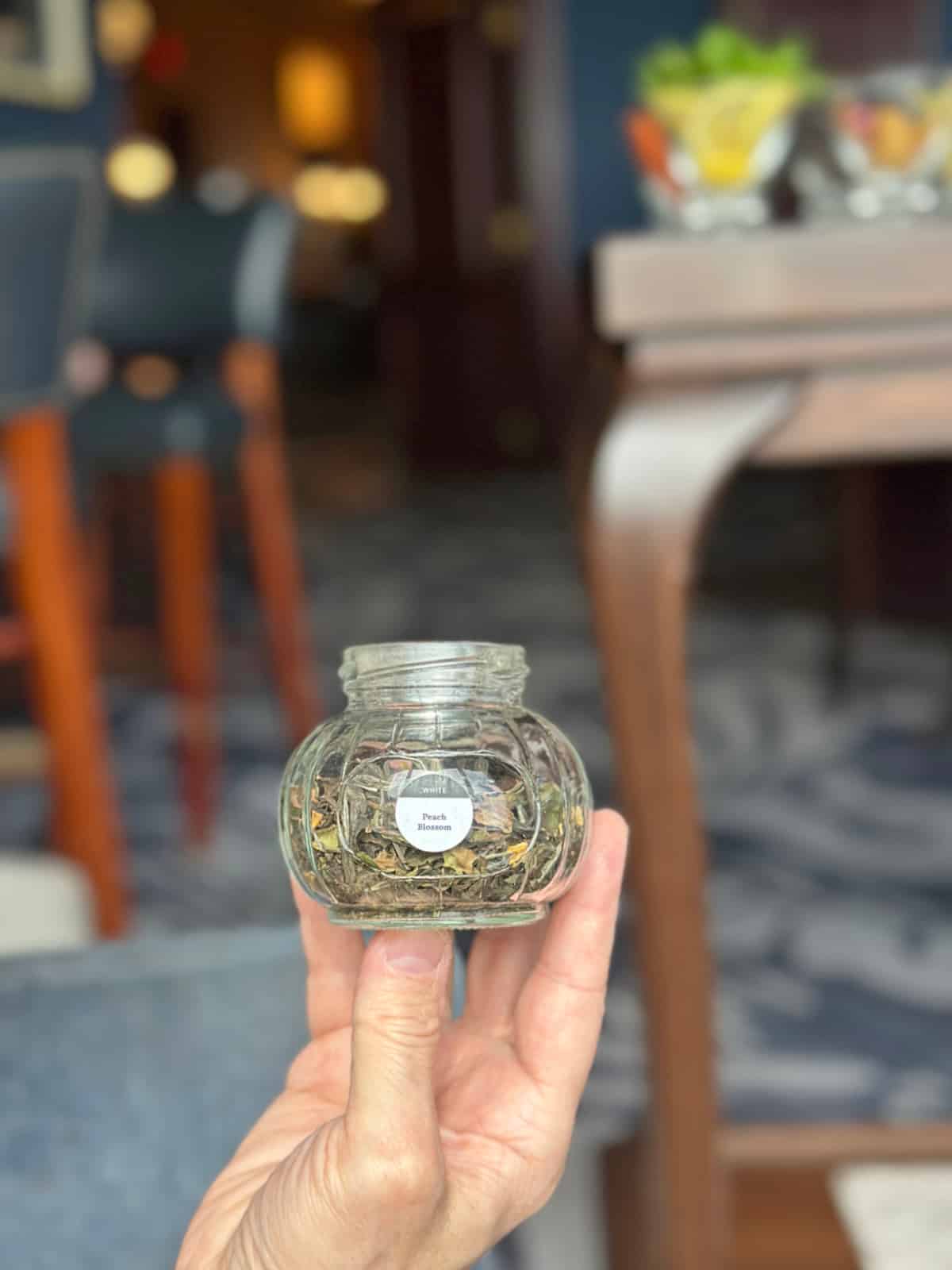 Hand holding glass container of peach blossom tea.