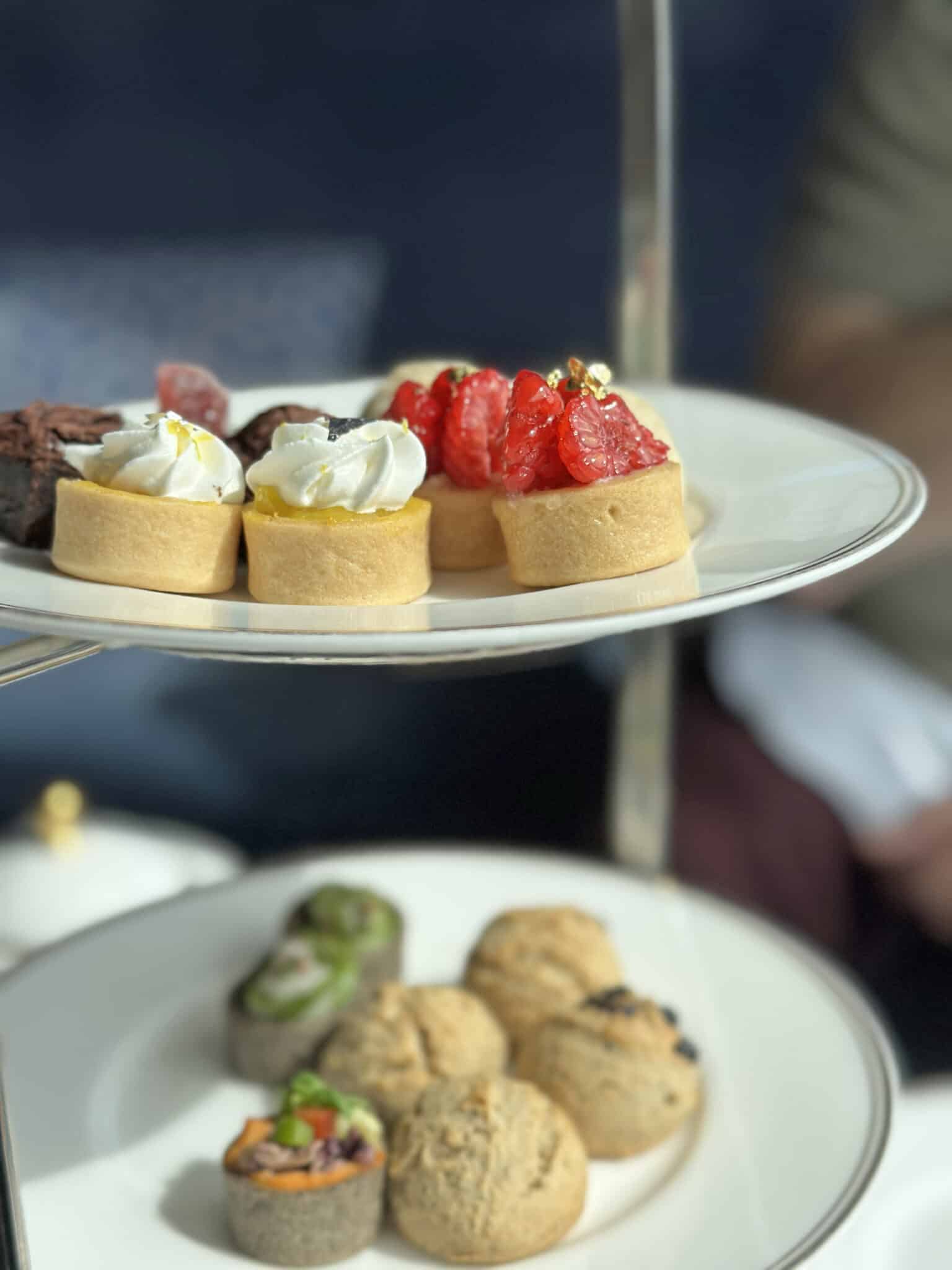 Lemon tarts, raspberry vegan cheese cake bites, and crumpets on plates.