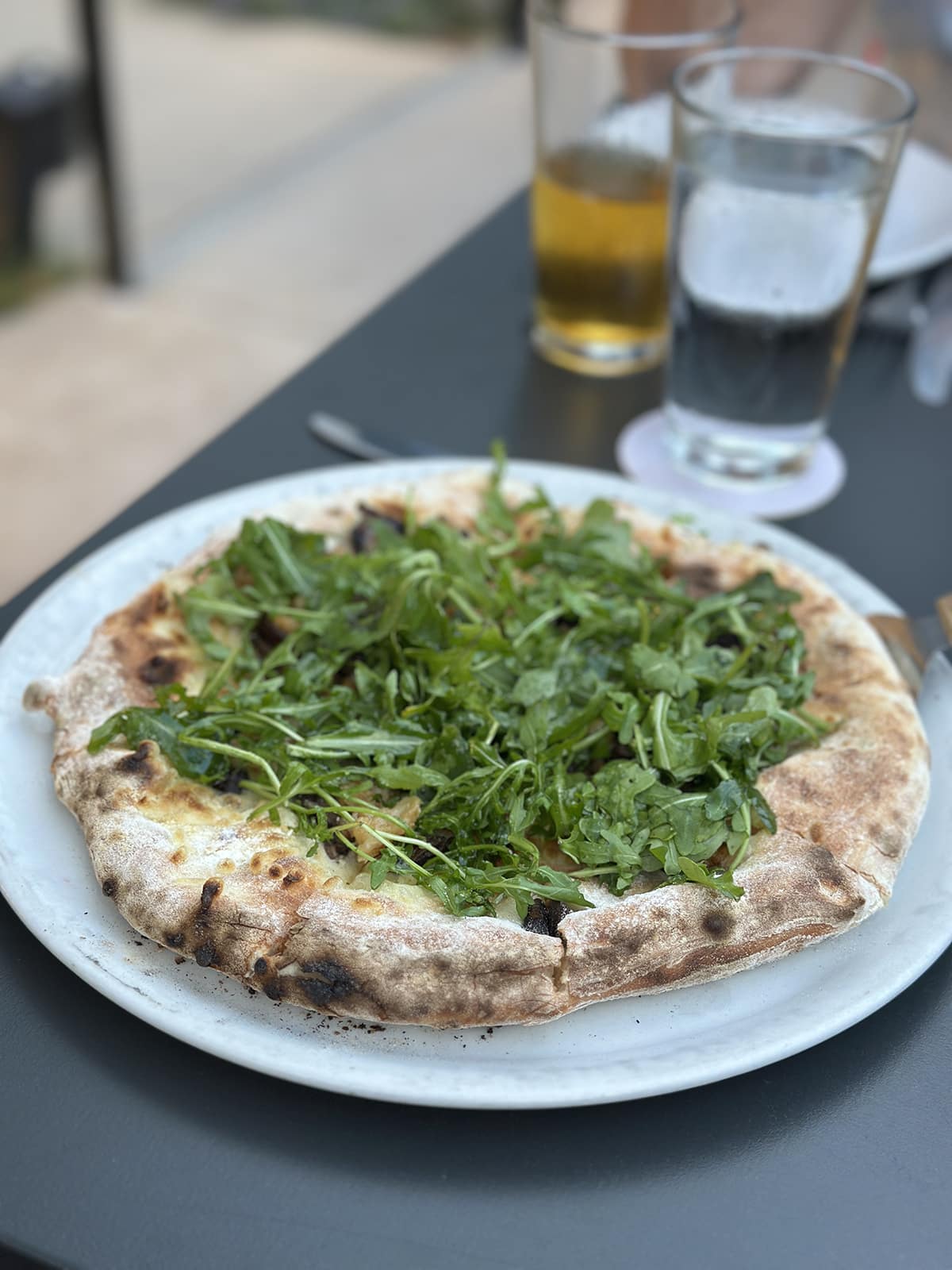 Funghi pizza at Maggie's Wood-fired Pizza with arugula, roasted garlic, vegan cheese, and mushrooms.