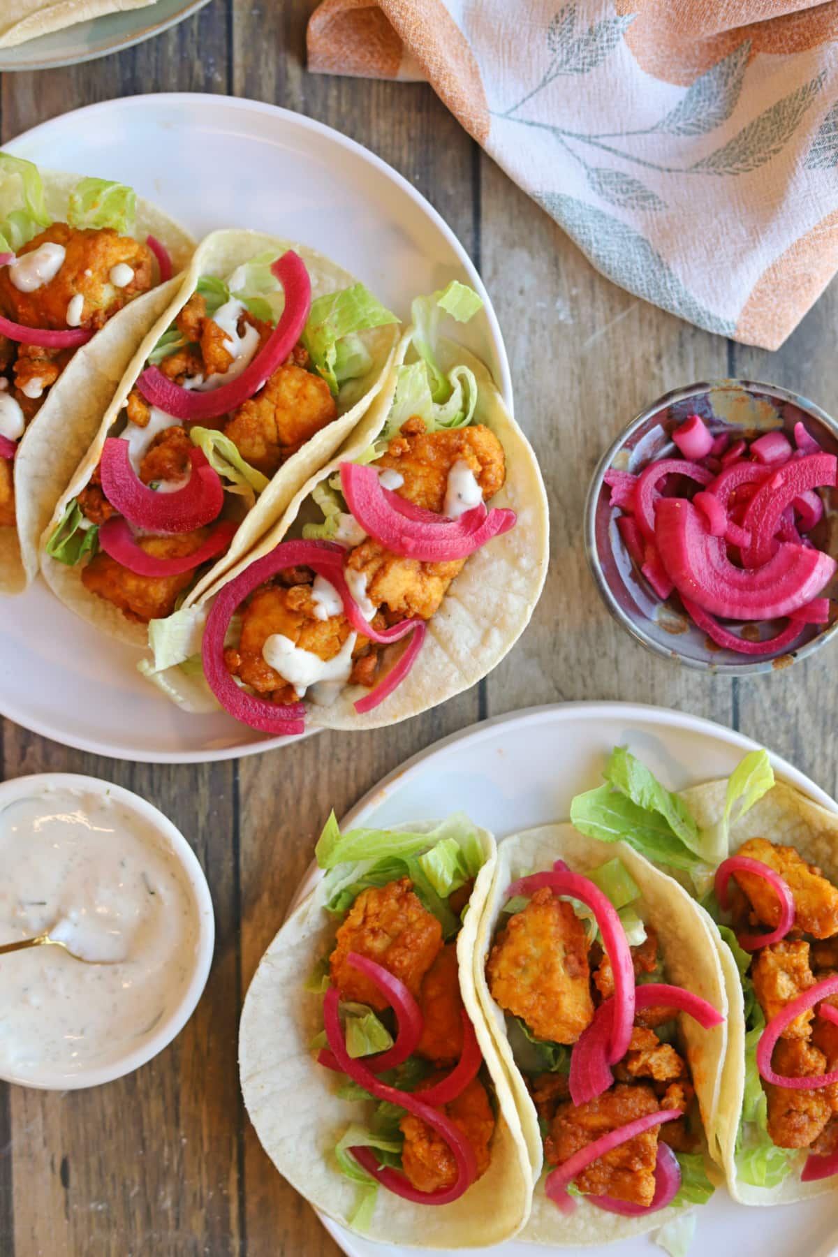 Table with buffalo tofu tacos, pickled red onions, and creamy onion and garlic dressing.
