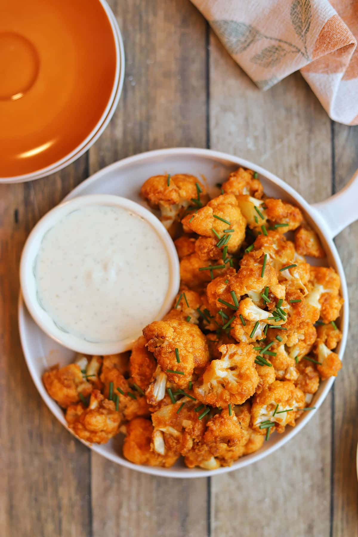 Buffalo cauliflower on plate with dipping sauce by orange plates.